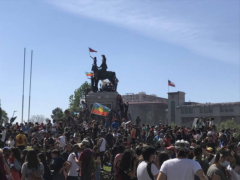 Manifestantes en Plaza Dignidad, banderas mapuche y chilena en el monumento
